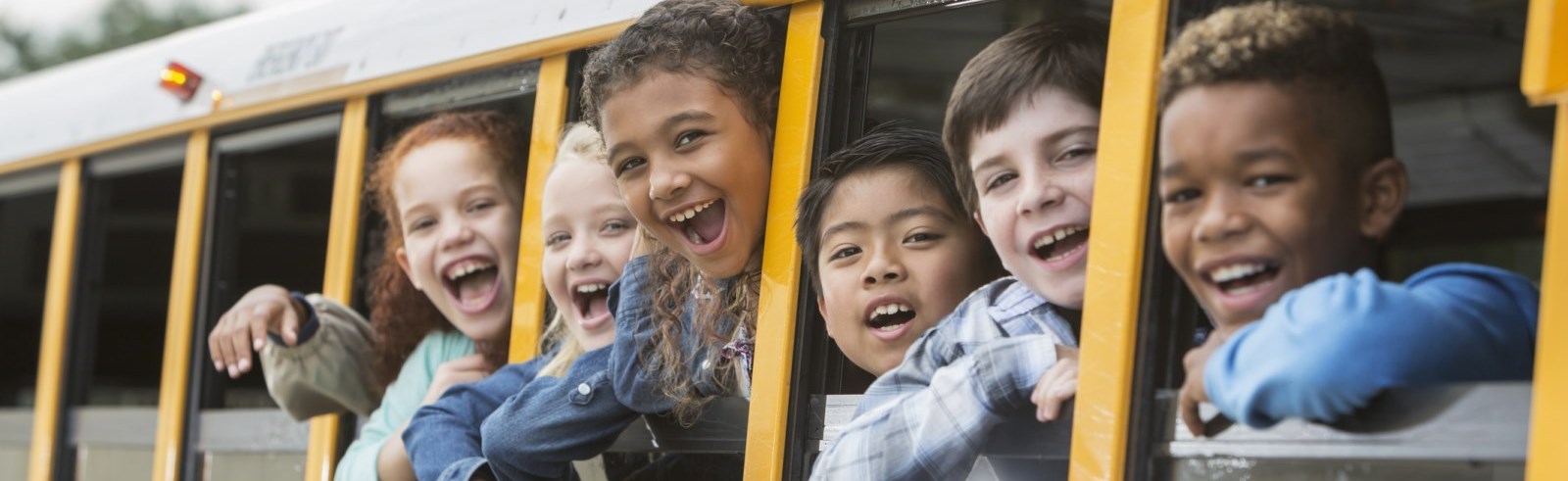 Children smiling with their heads out the bus windows